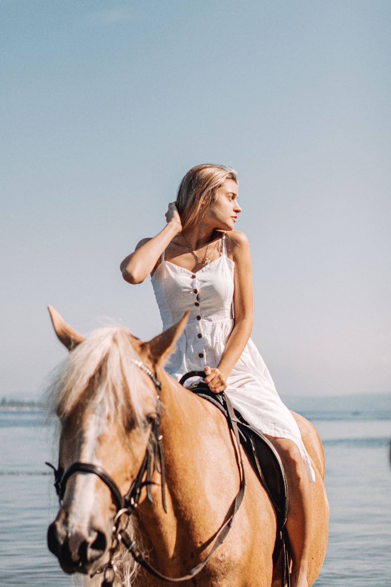 Woman riding a horse along the shoreline at sunset